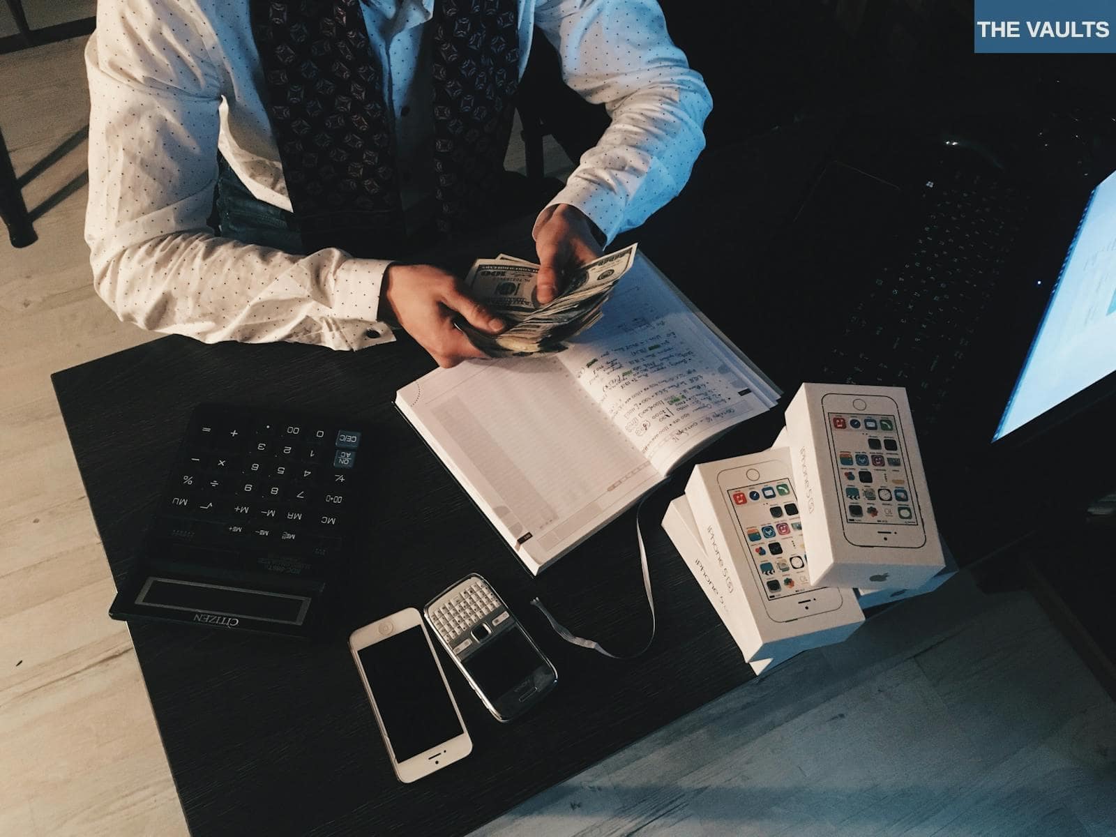 Businessman organizing finances with tech devices and cash on desk.