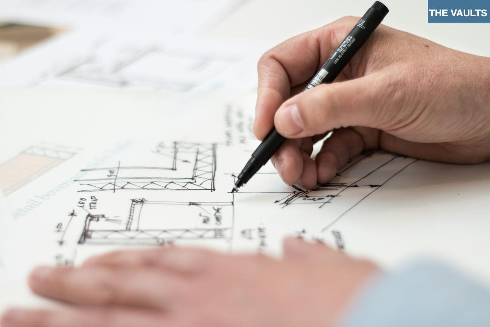 Close-up of hand drawing intricate technical designs on blueprint with pen, ideal for engineering or architecture themes.